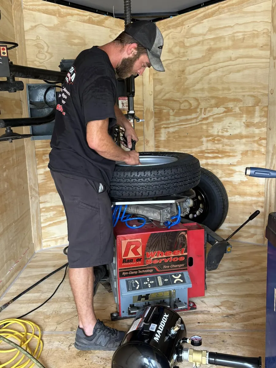 Michael Radford mounting a tire on a tire changer inside a plywood-lined trailer