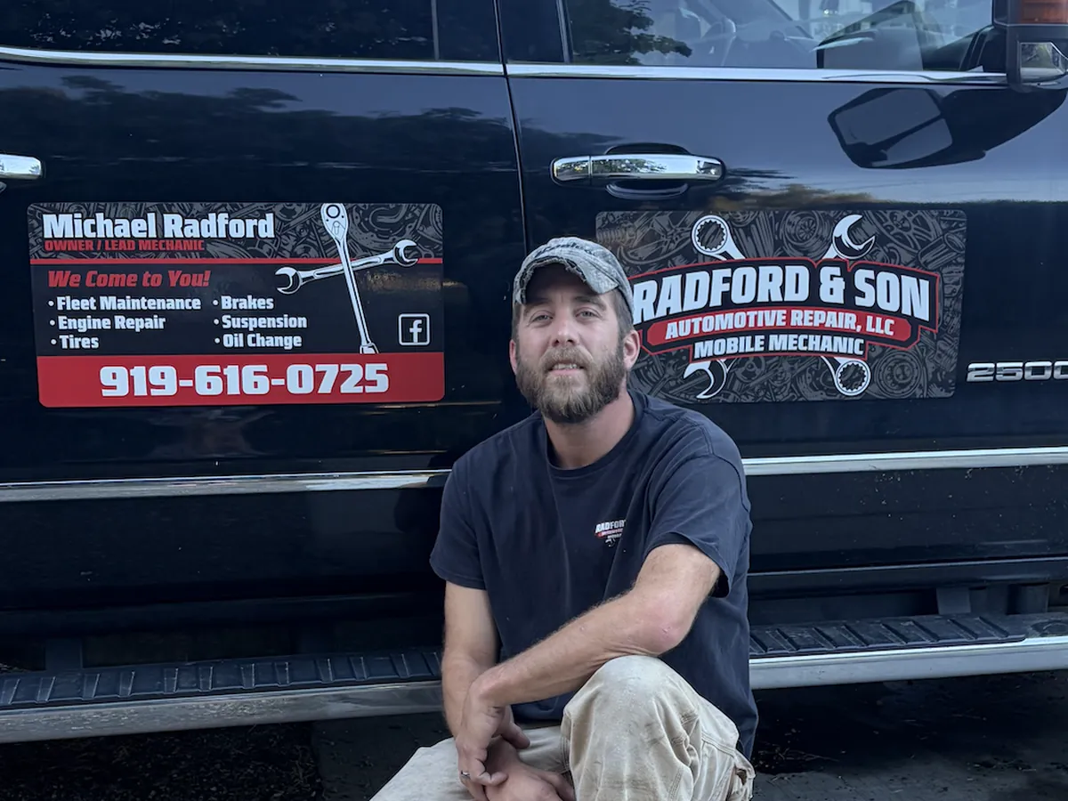 Michael Radford crouching beside his black pickup truck, which has Radford & Son door signs